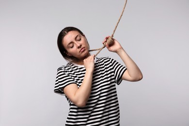 Photo of Depressed woman with rope noose on neck against light grey background