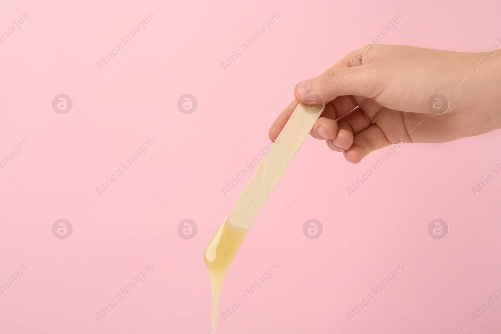 Photo of Woman holding spatula with hot depilatory wax on pink background, closeup. Space for text