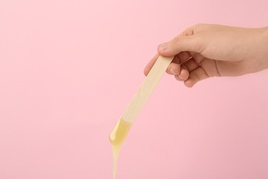 Woman holding spatula with hot depilatory wax on pink background, closeup. Space for text