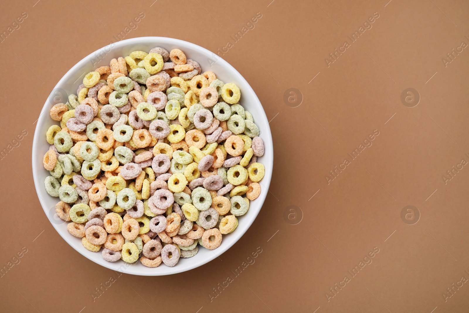 Photo of Tasty cereal rings in bowl on brown table, top view. Space for text