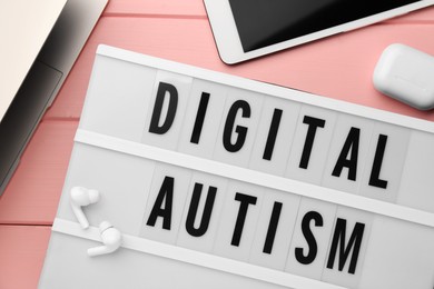 Photo of Lightbox with phrase Digital Autism and devices on pink wooden table, flat lay