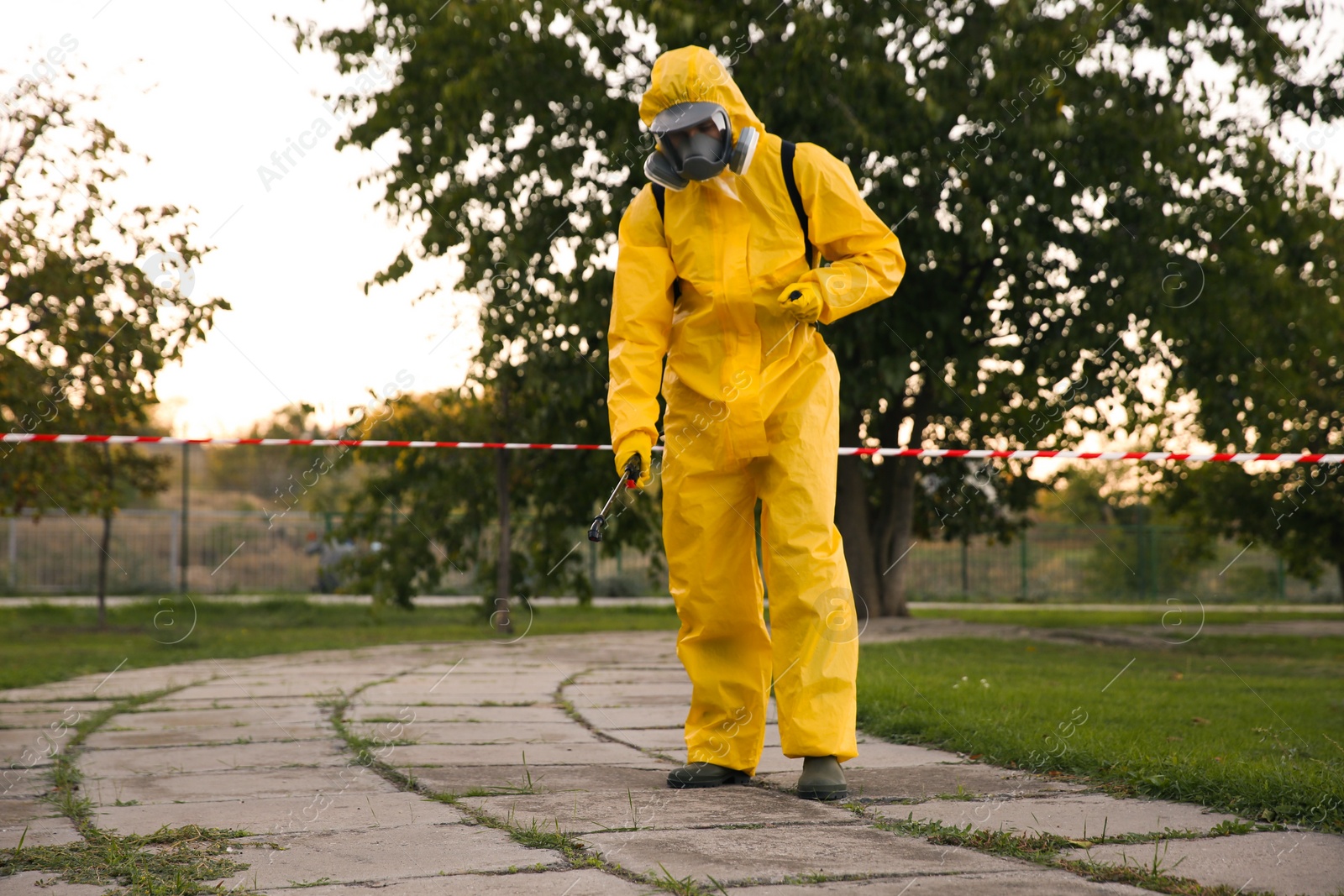 Photo of Person in hazmat suit disinfecting street pavement with sprayer. Surface treatment during coronavirus pandemic