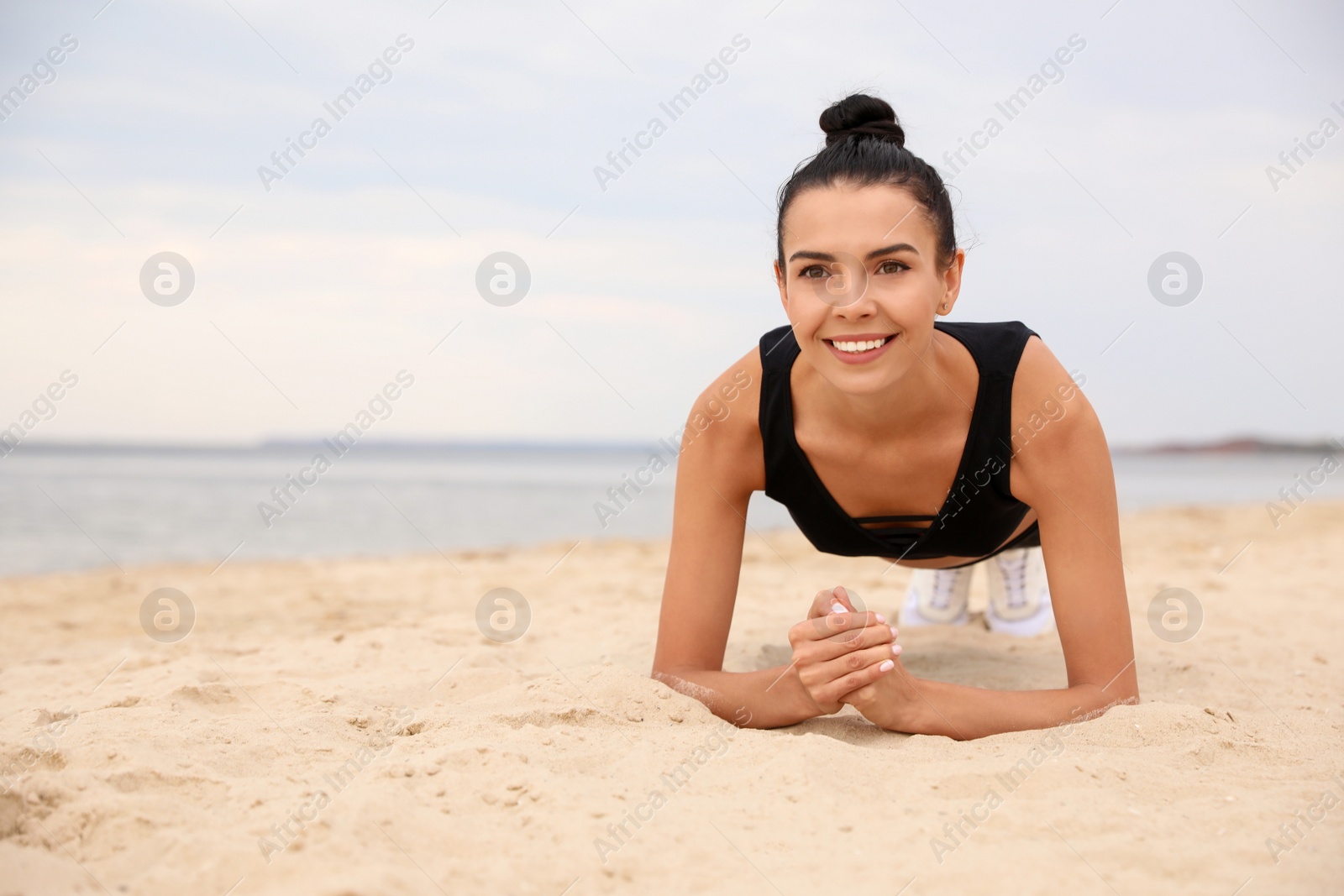 Photo of Young woman doing plank exercise on beach, space for text. Body training