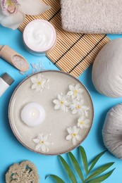 Photo of Beautiful composition with spa products, burning candle and flowers on light blue background, flat lay