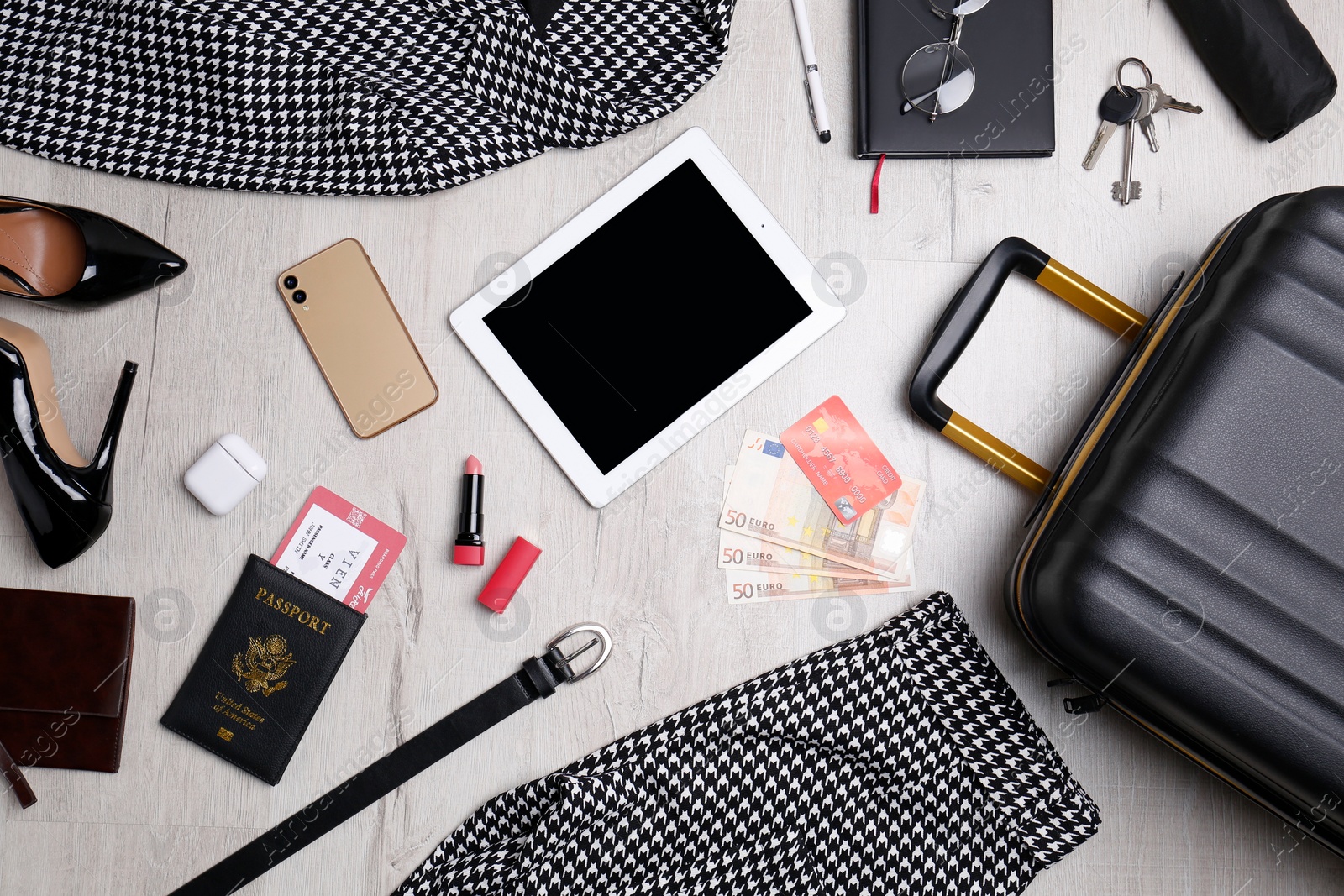 Photo of Business trip stuff and suitcase on light wooden surface, flat lay