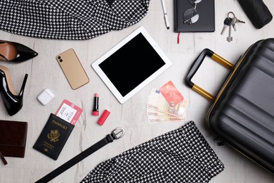 Business trip stuff and suitcase on light wooden surface, flat lay