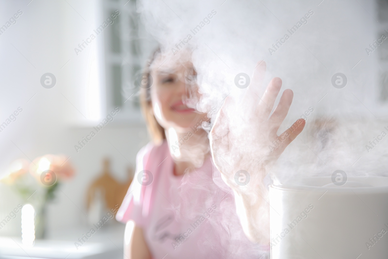 Photo of Woman near modern air humidifier in kitchen, focus on hand