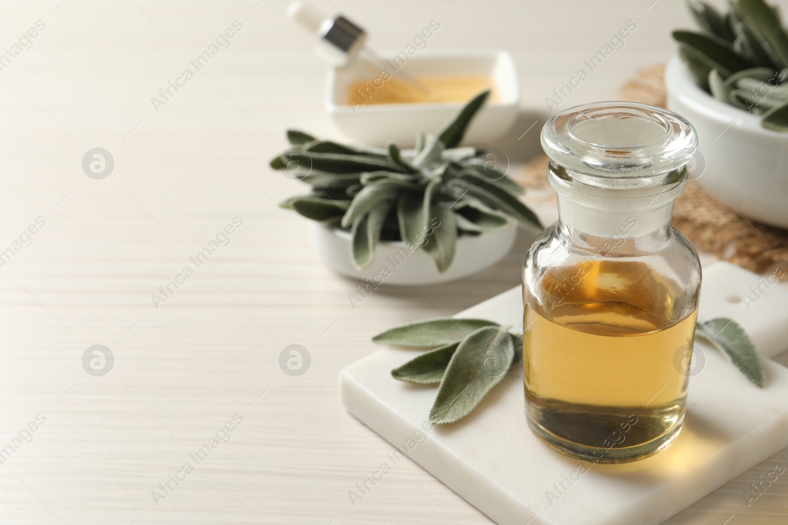 Photo of Bottle of essential sage oil and leaves on white wooden table. Space for text