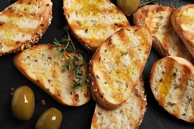 Photo of Tasty bruschettas with oil, thyme and olives on black table, flat lay