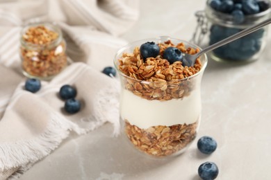 Photo of Glass of yogurt with granola and blueberries on grey marble table, closeup
