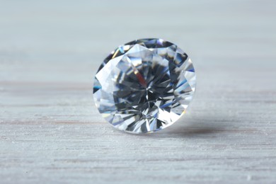 Photo of Beautiful shiny diamond on light wooden table, closeup