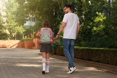 Father taking his daughter to school, back view