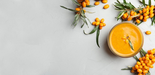 Image of Delicious sea buckthorn jam and fresh berries on light grey table, flat lay. Banner design with space for text