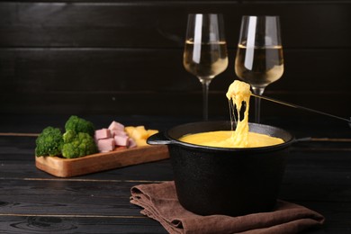 Photo of Dipping piece of ham into fondue pot with melted cheese on black wooden table