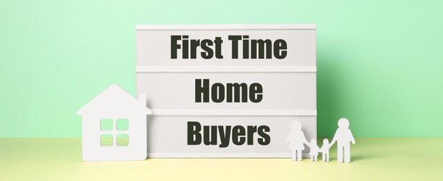 Image of First time home buyers. Lightbox, figures of family and house on table against green wall. Banner design