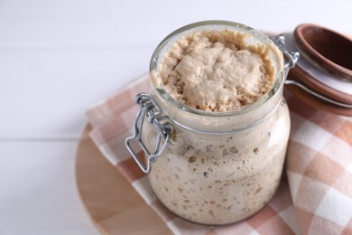 Photo of Sourdough starter in glass jar on white table, closeup. Space for text