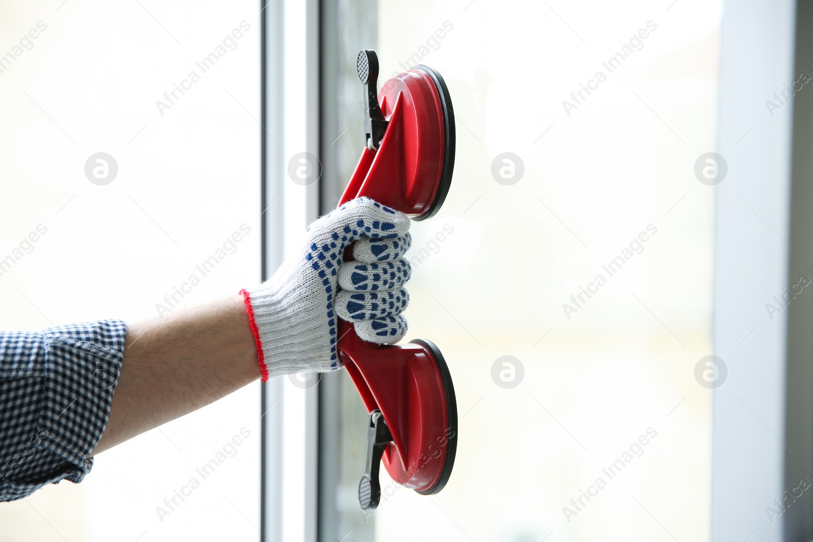 Photo of Construction worker using suction lifter during window installation indoors, closeup