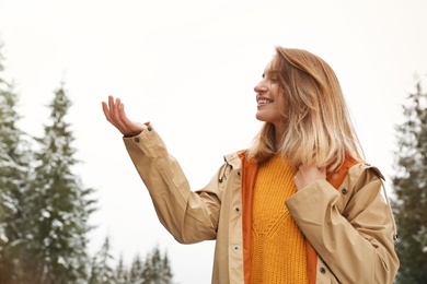 Young woman in warm clothes catching snow outdoors. Winter vacation