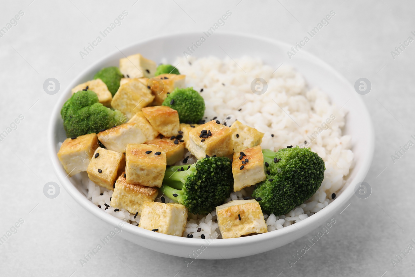 Photo of Bowl of rice with fried tofu and broccoli on white table, closeup