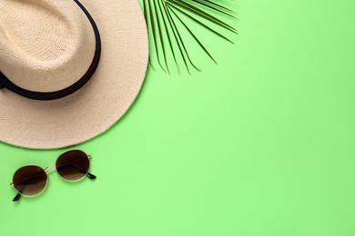 Photo of Stylish straw hat, sunglasses and palm leaf on light green background, flat lay. Space for text