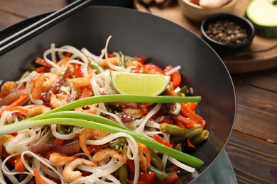 Photo of Shrimp stir fry with noodles and vegetables in wok on wooden table, closeup