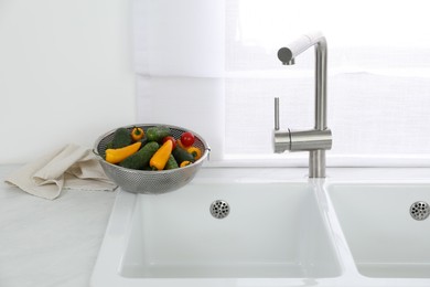 Photo of Modern sink with water tap and fresh vegetables near window in kitchen
