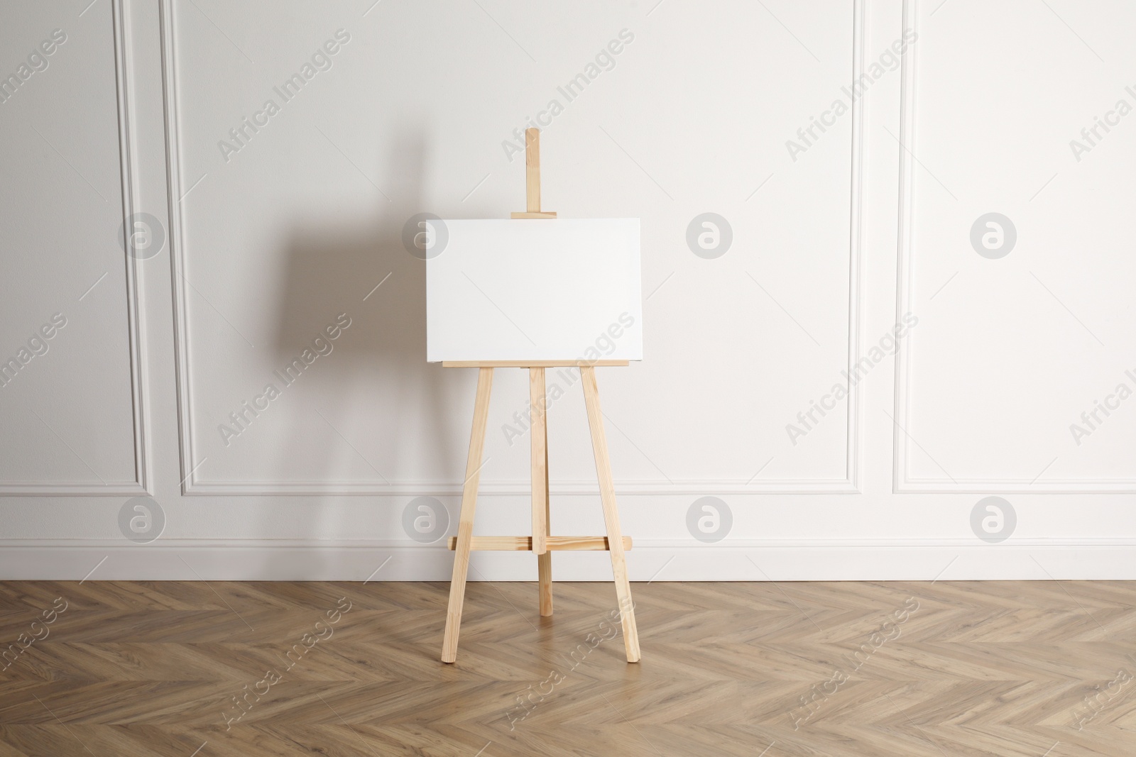 Photo of Wooden easel with blank canvas near light wall