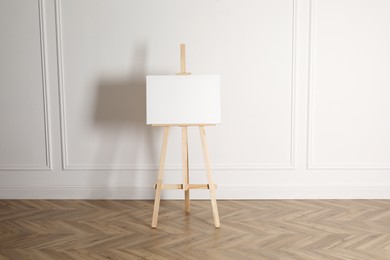 Photo of Wooden easel with blank canvas near light wall