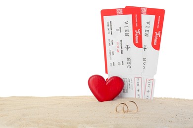 Photo of Honeymoon concept. Two golden rings, red wooden heart, tickets and sand isolated on white