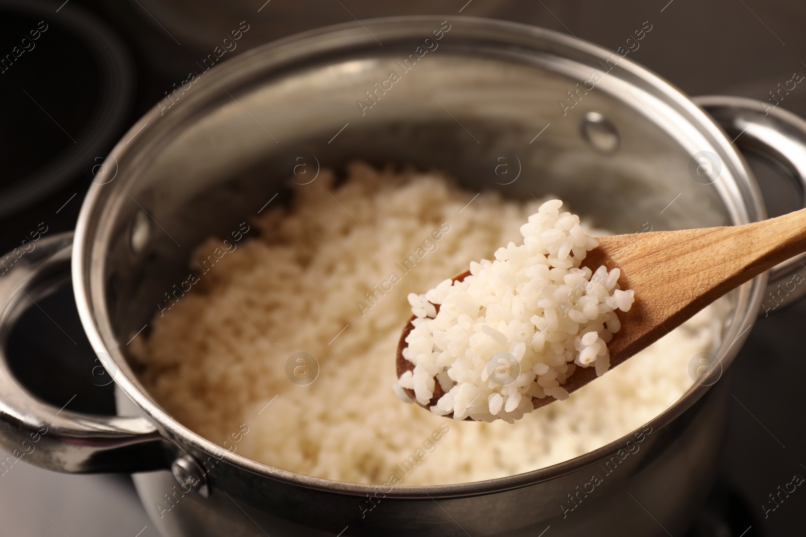 Photo of Wooden spoon with delicious rice over pot, closeup