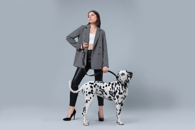 Beautiful young woman with her adorable Dalmatian dog on light grey background. Lovely pet