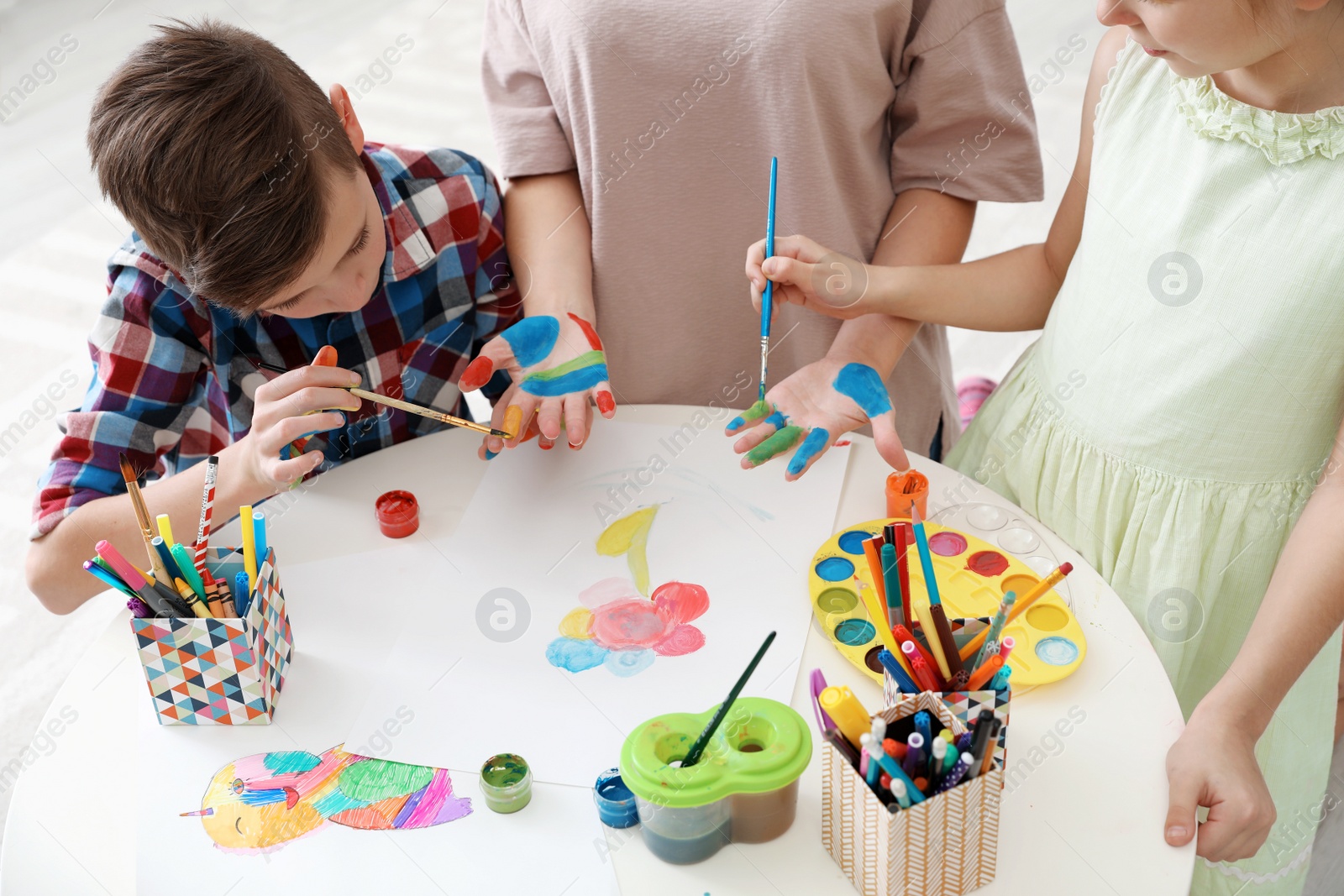 Photo of Young woman with children painting hands at table indoors, closeup view