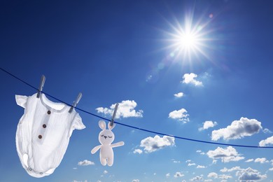 Baby onesie and crochet toy drying on washing line against sky