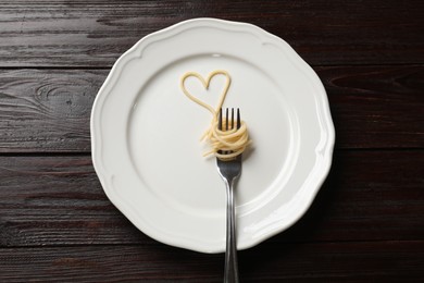 Photo of Heart made of tasty spaghetti and fork on wooden table, top view