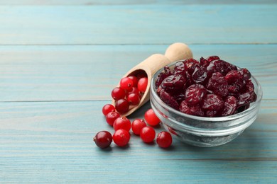 Photo of Tasty dried cranberries in bowl and fresh ones on light blue wooden table. Space for text