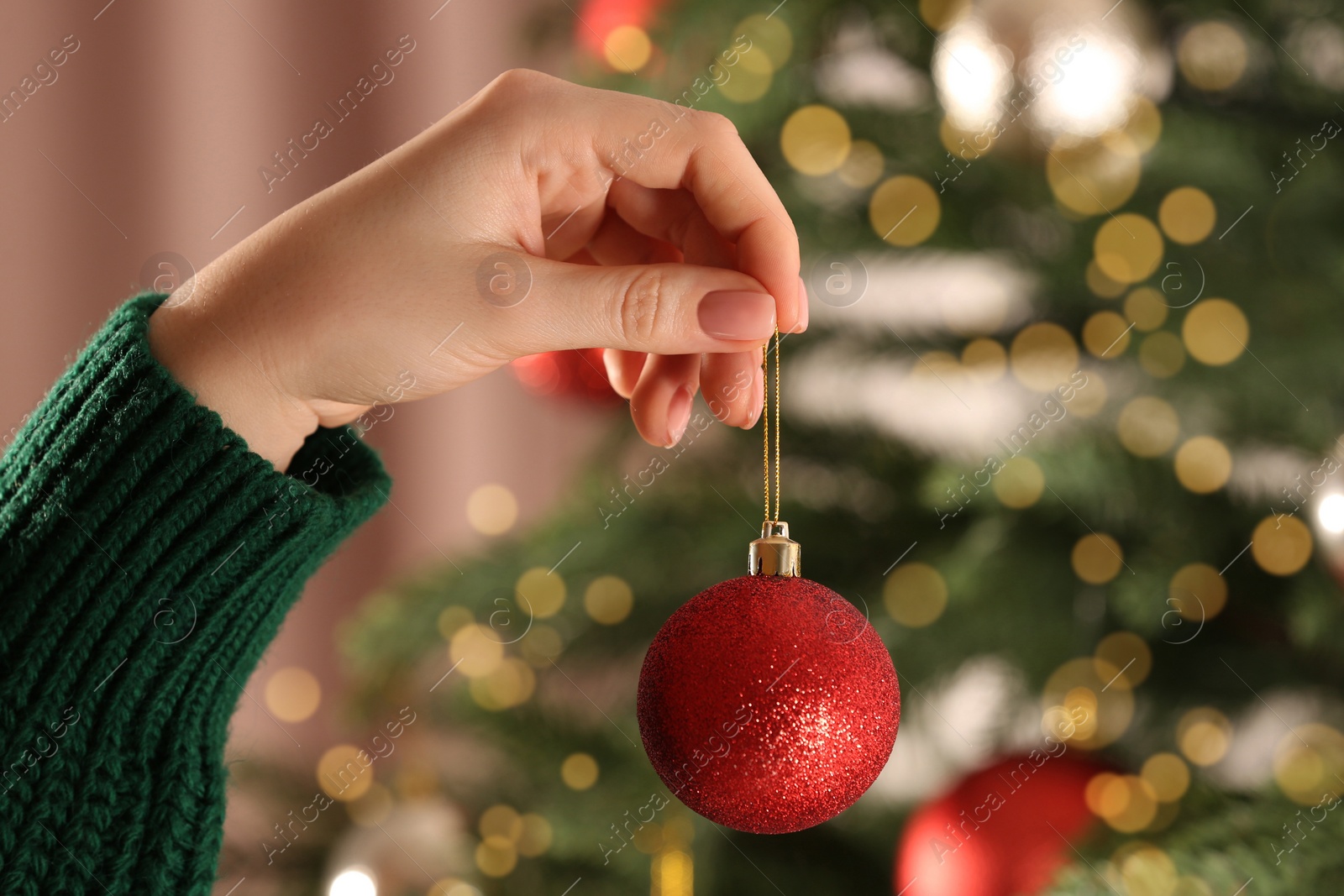 Photo of Woman holding beautiful red bauble near Christmas tree indoors, closeup