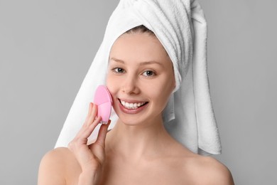 Washing face. Young woman with cleansing brush on grey background