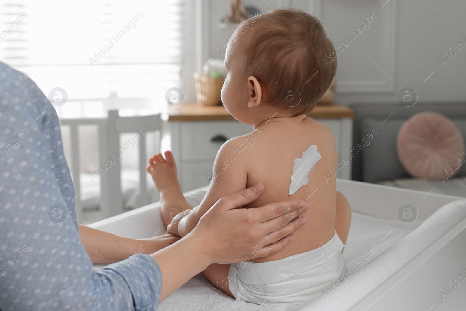 Photo of Mother applying body cream on her little baby at home, closeup