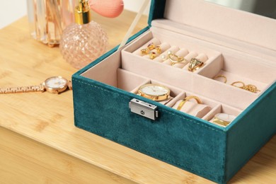 Jewelry box with many different accessories and perfume on wooden table, closeup