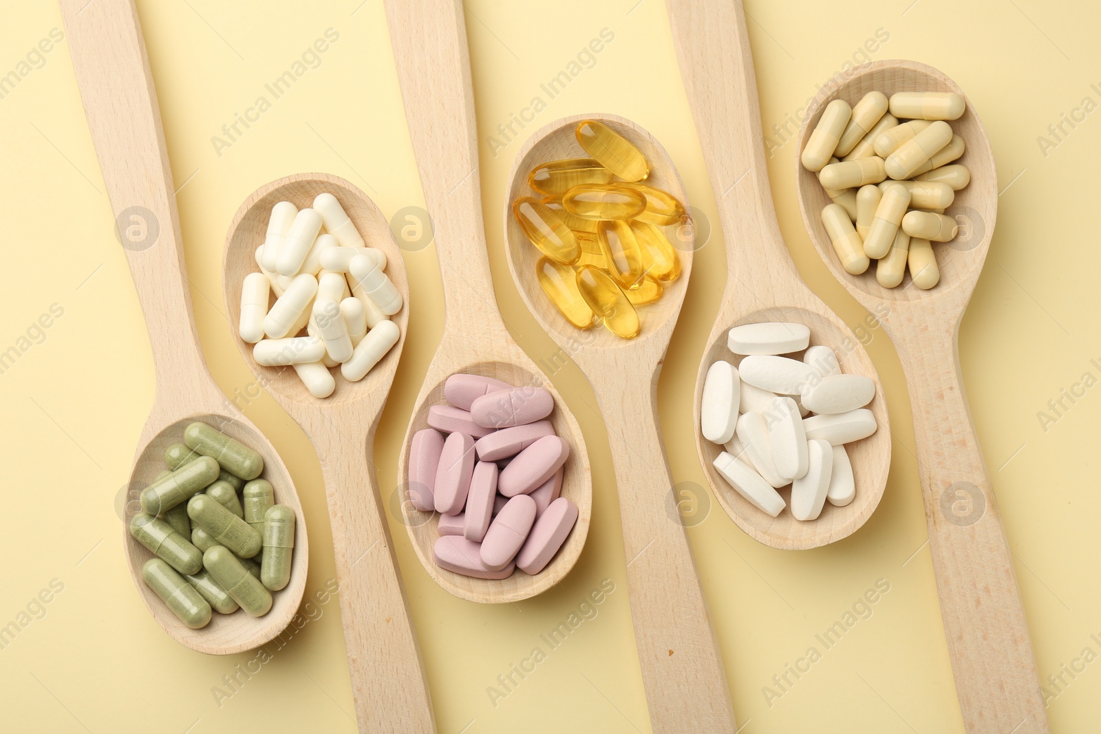 Photo of Different vitamin pills in spoons on pale yellow background, flat lay