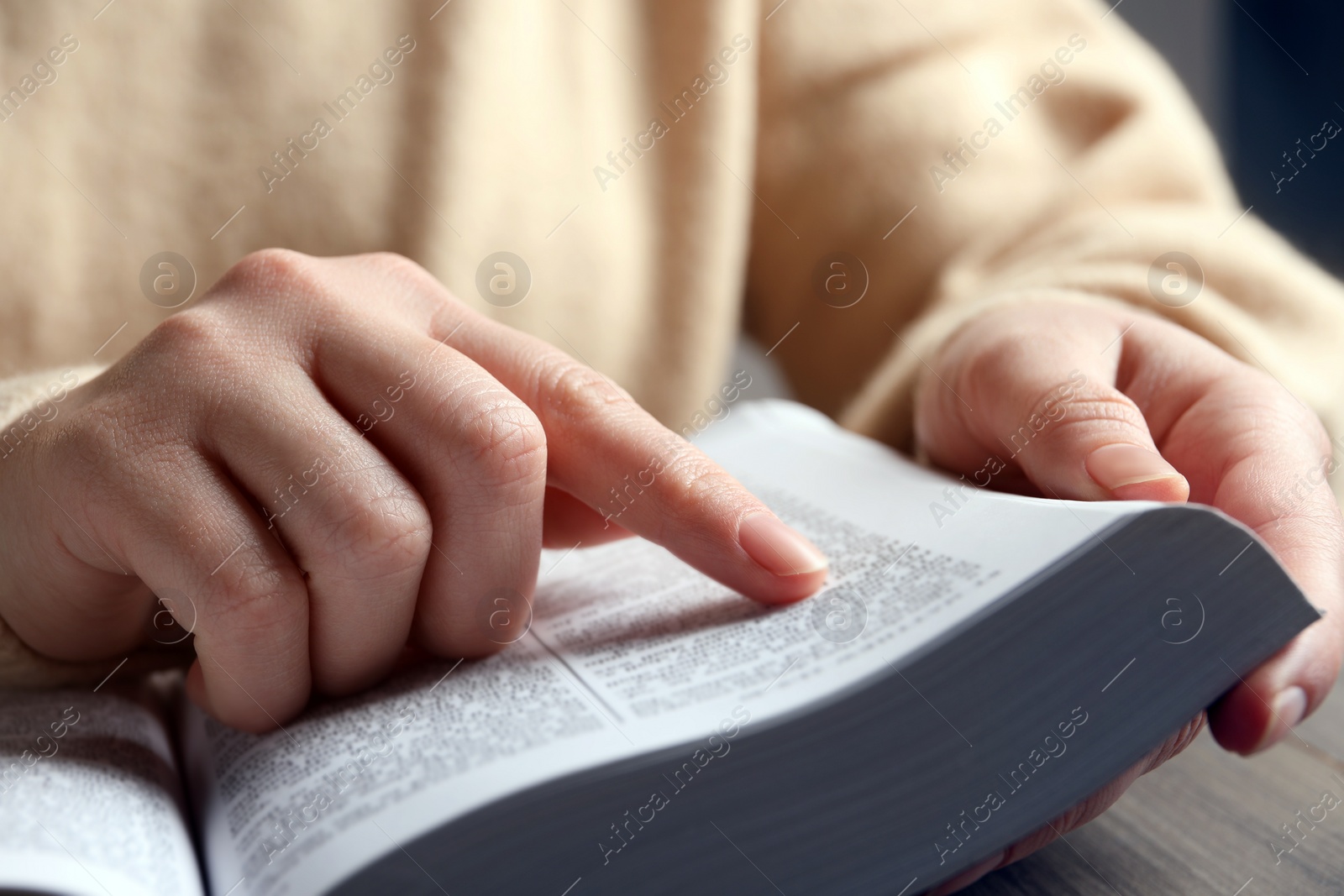 Photo of Woman reading Bible at wooden table, closeup