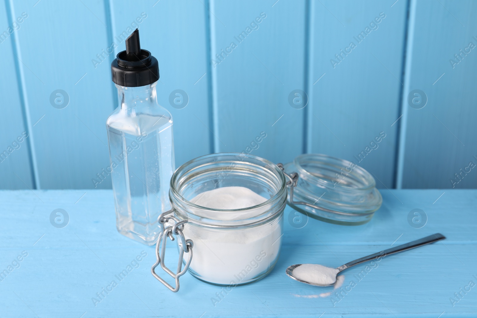 Photo of Natural cleaning products. Vinegar in bottle, baking soda and spoon on light blue wooden table