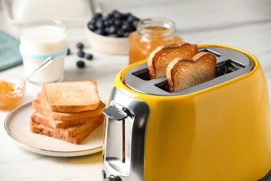 Yellow toaster with roasted bread slices, jam, blueberries and glass of milk on white table, closeup