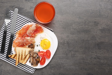 Photo of Plate with fried egg, bacon and vegetables on grey table