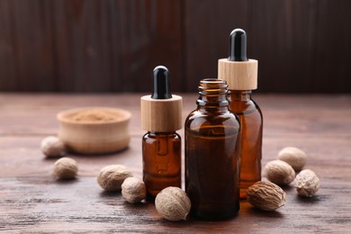 Bottles of nutmeg oil and nuts on wooden table