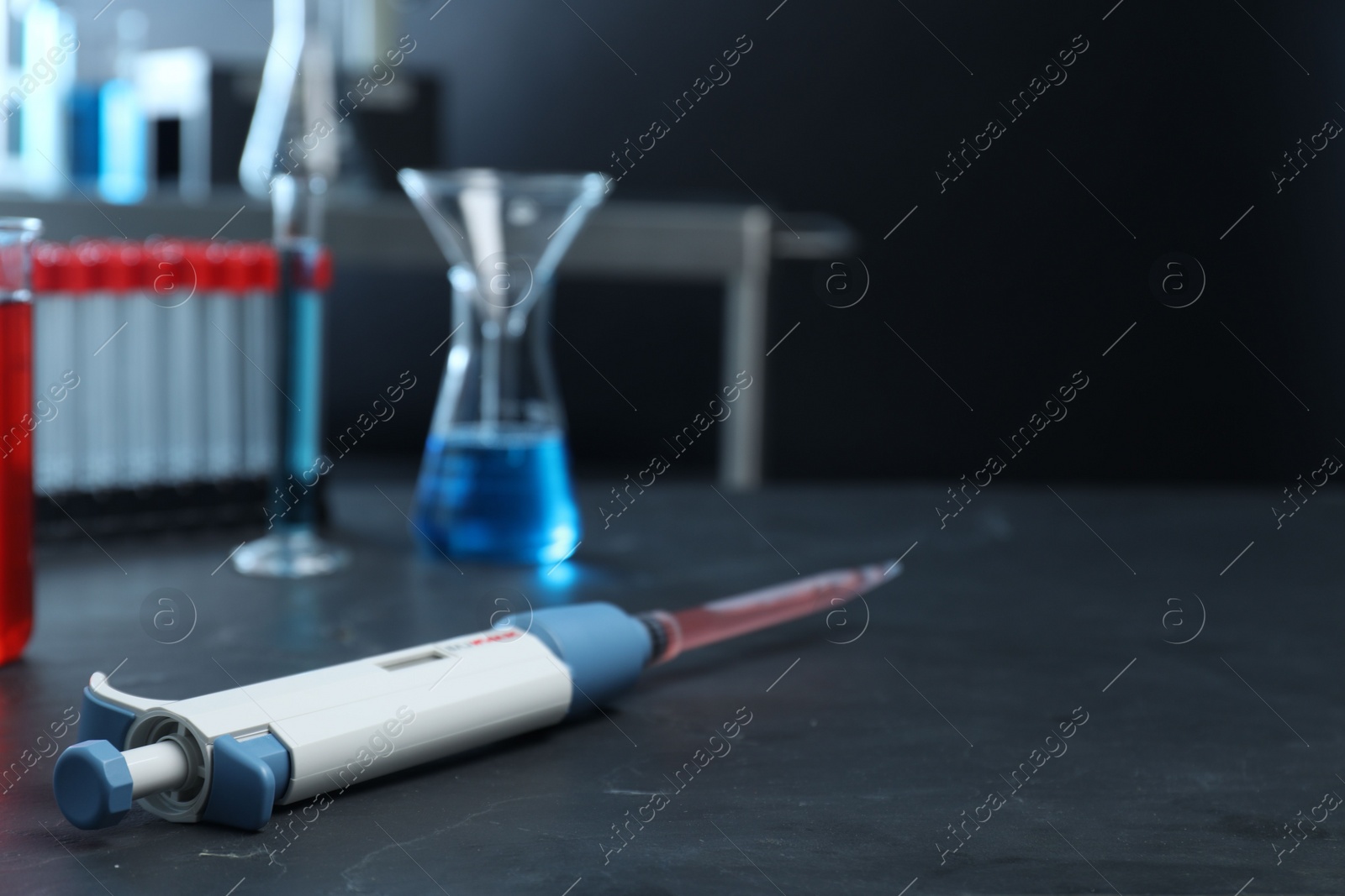 Photo of Laboratory analysis. Micropipette with liquid on black table, closeup. Space for text