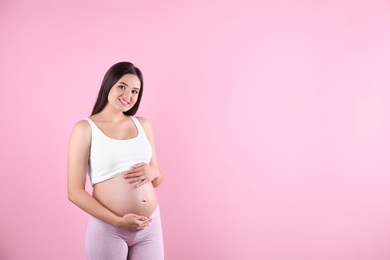 Photo of Beautiful pregnant woman holding hands on belly against color background. Space for text