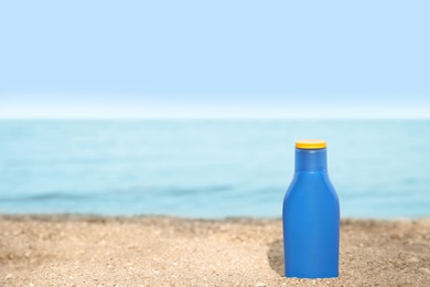 Photo of Bottle of sun protection body cream on beach, space for design