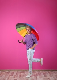 Man with rainbow umbrella near color wall