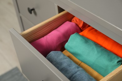 Photo of Different rolled shirts in drawer indoors. Organizing clothes
